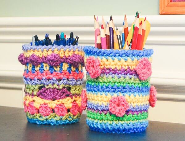 Colorful crochet mason jar cozies used as pen and pencil holders on a desk